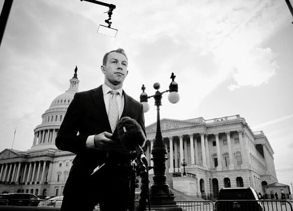Photo of individual speaking to cameras with Capitol Hill in the background.
