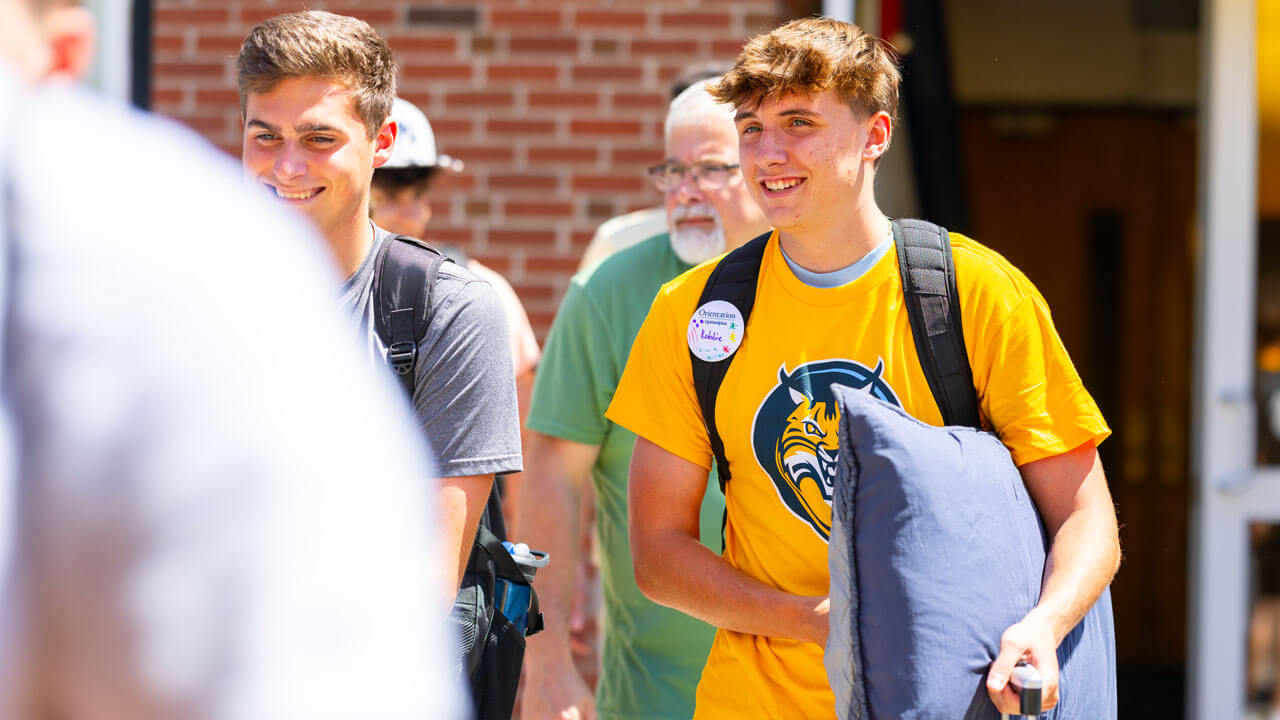 Individual walks out of the Recreation and Wellness Center carrying a backpack and a pillow.