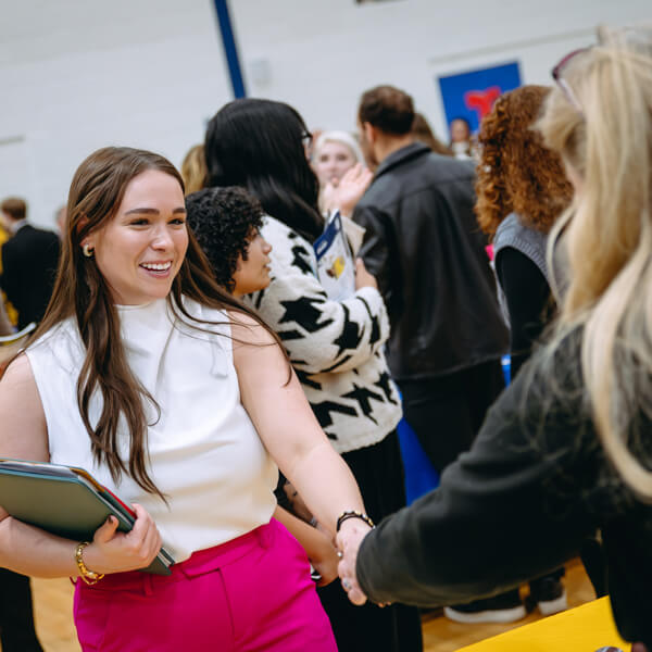 A Quinnipiac student in professional attire shakes hands with a woman at a career fair.